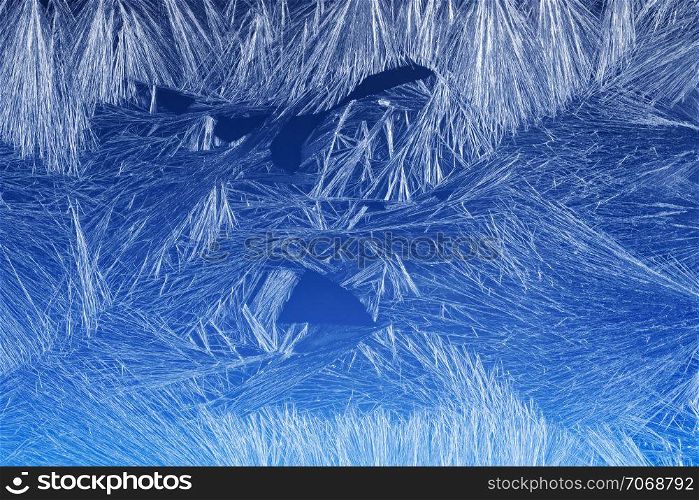 Textures and backgrounds: ice crystals on the window, frost texture over the blue sky gradient. Abstract winter pattern, seasonal background.. Frost pattern on a window glass