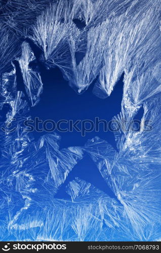 Textures and backgrounds: ice crystals on the window, frost texture over the blue sky gradient. Abstract winter pattern, seasonal background.. Frost pattern on a window glass