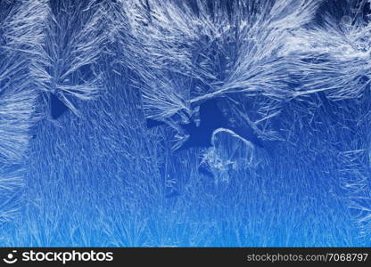 Textures and backgrounds: ice crystals on the window, frost texture over the blue sky gradient. Abstract winter pattern, seasonal background.. Frost pattern on a window glass