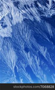 Textures and backgrounds: ice crystals on the window, frost texture over the blue sky gradient. Abstract winter pattern, seasonal background.. Frost pattern on a window glass