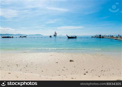 Thai boats in the sea near the pontoon in sunny weather, view from the beach of the island of Hong