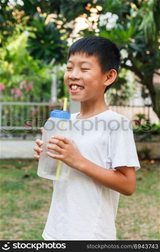 Thai boy drink cold water from plasctic bottle using straw.