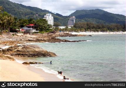 Thai children are swimming in the wild beach. In the background, Patong beach and modern hotels. Editorial only.