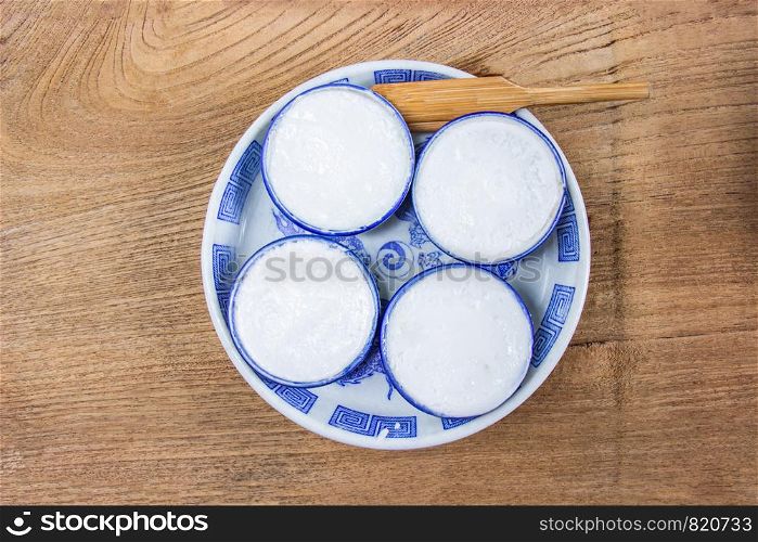 Thai Coconut Milk Custard is a thai dessert made from rice flour, coconut milk and sugar put the small ceramic cups place are on a wooden floor. Khanom Thuai,