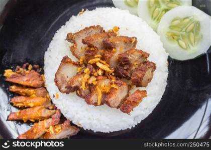 Thai Food Fried Pork with Garlic and Cucumber in Black Dish Top view. Fried pork with garlic or steak on rice and cucumber in food and drink category flatray or top table view