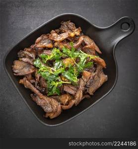 Thai food, fried sun dried beef with crispy basil leaves in black pan on the dark tone texture background