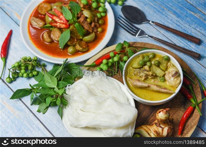 Thai food green curry on soup bowl and red curry on white plate with thai rice noodles ingredient herb vegetable on wooden background / green curry chicken cuisine asian food on the table