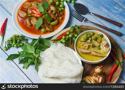 Thai food green curry on soup bowl and red curry on white plate with thai rice noodles ingredient herb vegetable on wooden background / green curry chicken cuisine asian food on the table