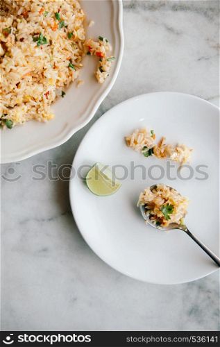 Thai fried rice in white dish and in spoon on side plate with marble table background - Top view shot