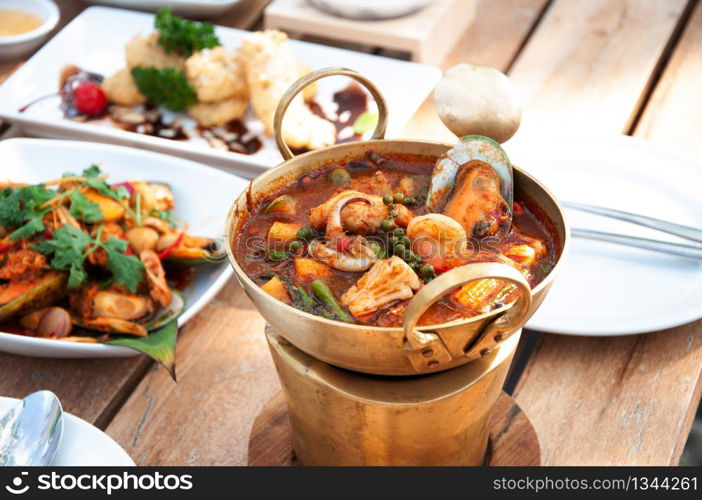 Thai hot and spicy seafood curry with vegetable and herbs or Kaeng Pa in brass bowl on mini stove at lunch table.