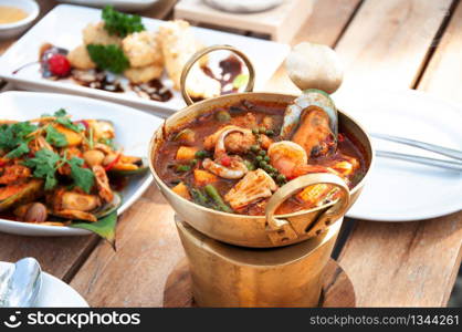 Thai hot and spicy seafood curry with vegetable and herbs or Kaeng Pa in brass bowl on mini stove at lunch table.