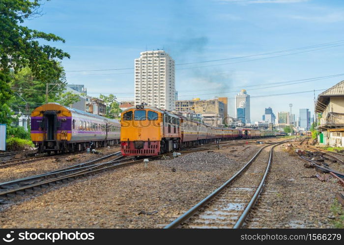 Thai local old classic train or tram on railway in Hua Lamphong terminal station with skyscraper high rise buildings in urban city, Bangkok town, Thailand in public transportation concept.