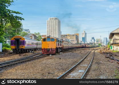 Thai local old classic train or tram on railway in Hua Lamphong terminal station with skyscraper high rise buildings in urban city, Bangkok town, Thailand in public transportation concept.