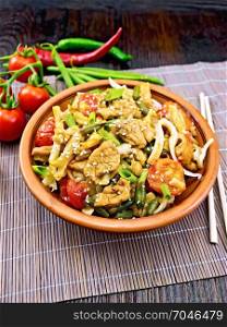Thai noodles wok with chicken meat, tomatoes, soy sauce and green beans sprinkled with sesame seeds in a plate on a bamboo napkin on a wooden board background