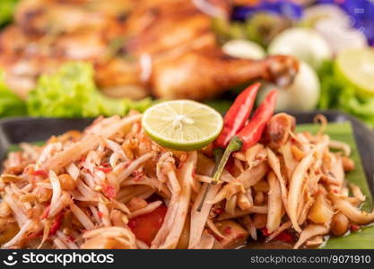 Thai papaya salad in a black plate consisting of papaya, chili, tomatoes, peanuts, and lime.