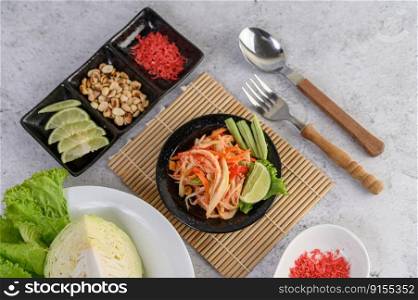 Thai papaya salad in a white plate with Spoon, fork, and dried shrimp.