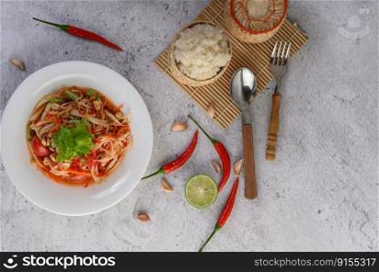 Thai papaya salad in a white plate with Sticky rice, chili, Spoon, and fork.