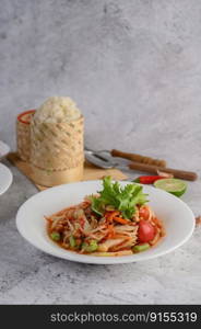 Thai papaya salad in a white plate with Sticky rice, chili, Spoon, and fork.