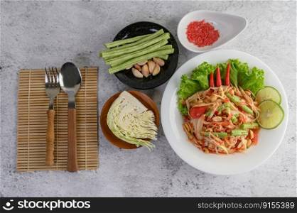 Thai papaya salad in a white plate with Sticky rice, dried shrimp, Spoon, and fork.