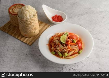 Thai papaya salad in a white plate with Sticky rice in wicker basket bamboo and dried shrimp.