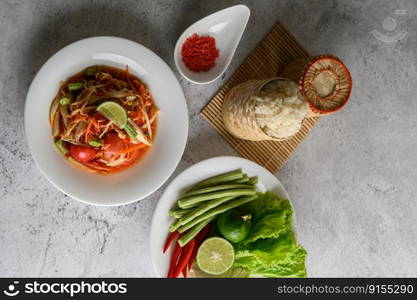 Thai papaya salad in a white plate with Sticky rice in wicker basket bamboo and dried shrimp.