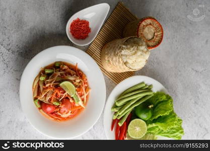 Thai papaya salad in a white plate with Sticky rice in wicker basket bamboo and dried shrimp.