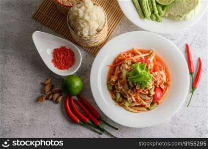 Thai papaya salad in a white plate with Sticky rice in wicker basket bamboo and dried shrimp.