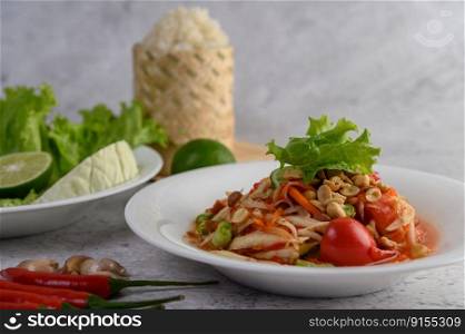Thai papaya salad in a white plate with Sticky rice in wicker basket bamboo.