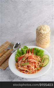 Thai papaya salad in a white plate with Sticky rice, Spoon, and fork.