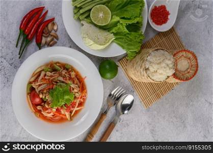Thai papaya salad in a white plate with Sticky rice, Spoon, fork, and dried shrimp.