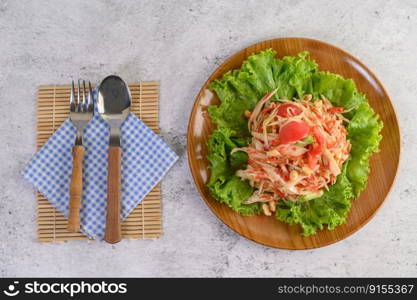 Thai papaya salad in a wooden plate with Spoon, and fork.