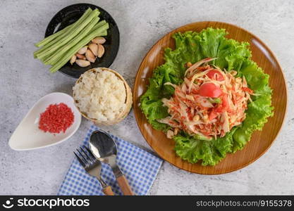 Thai papaya salad in a wooden plate with Sticky rice, Spoon, and fork.