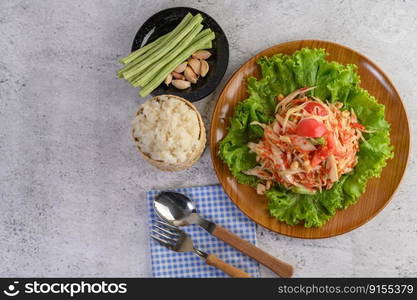 Thai papaya salad in a wooden plate with Sticky rice, Spoon, and fork.