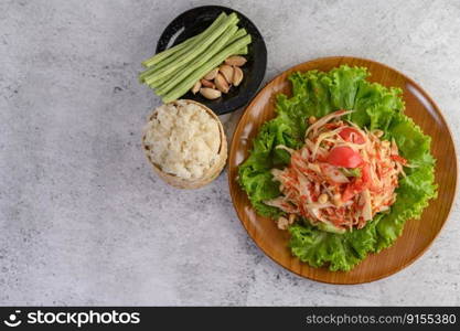 Thai papaya salad on salad in a wooden plate with Sticky rice, Yardlong beans, and garlic. Top view.