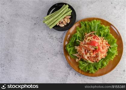 Thai papaya salad on salad in a wooden plate with Yardlong beans and garlic, Top view.