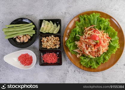 Thai papaya salad on salad in a wooden plate with Yardlong beans and garlic, Top view.