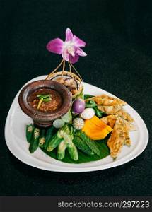 Thai spicy shrimp paste chili dip in mortar cup with assorted vegetables and fried egg on black table