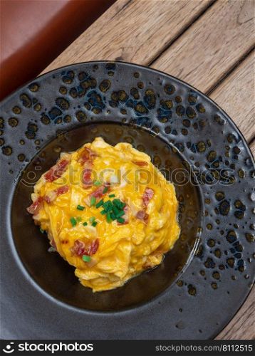 Thai style omelet with bacon and spring onions in black ceramic plate on wooden table. Creamy Thai omelet on the black ceramic dish.Thai food, food concept. Flat-lay, top-down, copy space.