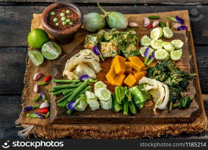 Thai Traditional Local Food : Spicy Shrimp Paste Dip or Fried shrimp paste sauce (Nam Prik Kapi) with blanched vegetables and cha-om omelets on wooden backgroud.