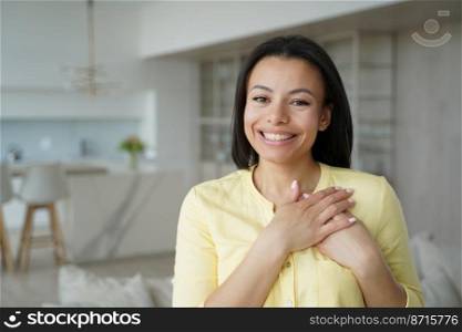 Thankful smiling peaceful woman keep hands close to heart, feeling gratefulness, appreciation, hope, standing alone at home. Emotional young female expressing deep gratitude, happy with good deed.. Thankful female keep hands close to heart, feel gratitude, appreciation happy with good deed at home