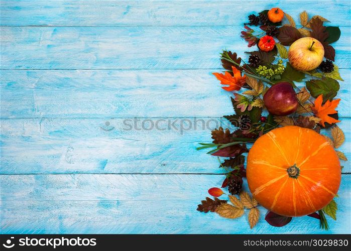 Thanksgiving background with leaves and squash on blue wooden . Happy Thanksgiving greeting with squash, apples and autumn leaves on theright side of blue wooden table. Fall background with seasonal vegetables and fruits, copy space