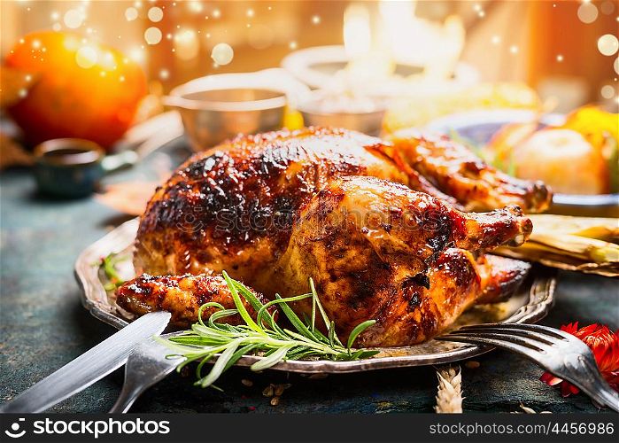 Thanksgiving day dinner table setting with whole roasted turkey or chicken on plate with cutlery , festive lighting and decoration, close up