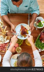thanksgiving day, eating and leisure concept - couple having roast chicken or turkey for dinner at table with food. group of people eating chicken for dinner
