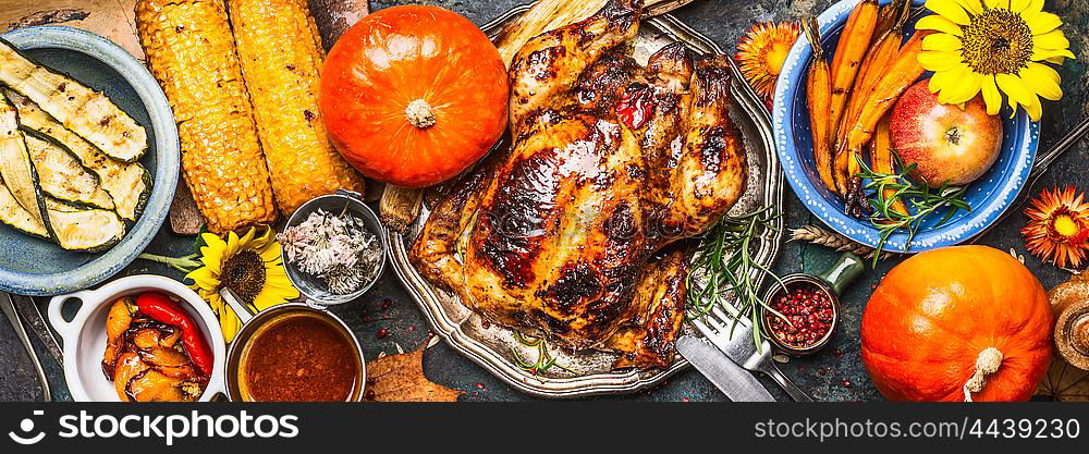 Thanksgiving Day food. Various grilled vegetables ,roasted chicken or turkey and pumpkin with sunflowers decoration on dark background, top view, banner