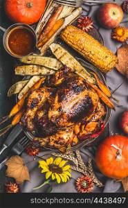 Thanksgiving Day roasted whole stuffed chicken or turkey served with sauce ,corn and vegetables on kitchen table decorated with flowers , pumpkins and autumn flowers, top view