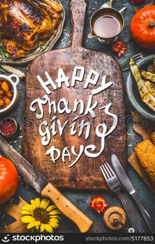 Thanksgiving dinner background with turkey ,sauce,grilled vegetables,corn ,cutlery , pumpkin, fall leaves and text Happy Thanksgiving Day on wooden gutting board, top view.