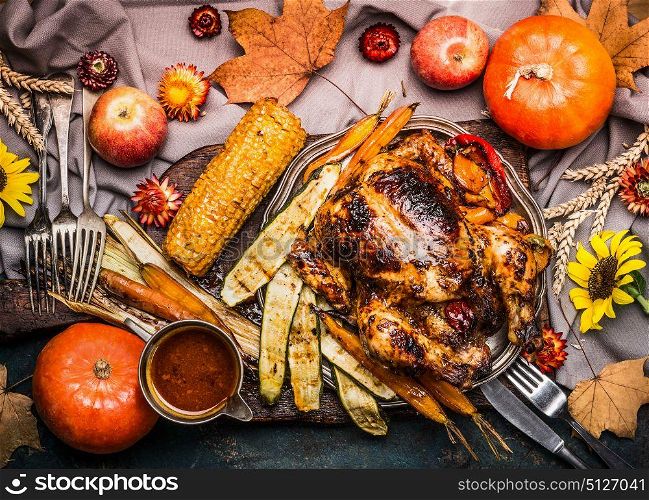 Thanksgiving dinner table with Roasted whole turkey ,sauce with grilled autumn vegetables,corn ,cutlery , decoration pumpkin, autumn leaves and flowers arrangements on rustic background, top view.