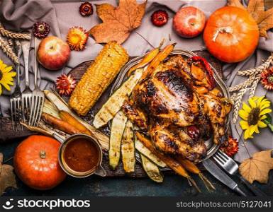 Thanksgiving dinner table with Roasted whole turkey ,sauce with grilled autumn vegetables,corn ,cutlery , decoration pumpkin, autumn leaves and flowers arrangements on rustic background, top view.