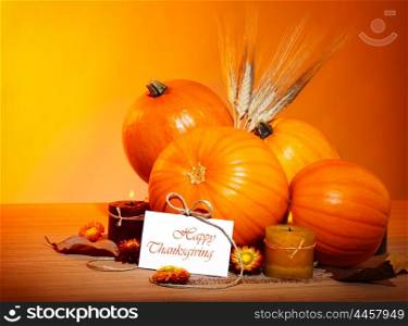 Thanksgiving holiday, pumpkin still life decoration with candles and wheat over yellow studio light background, greeting card with text space, harvest concept