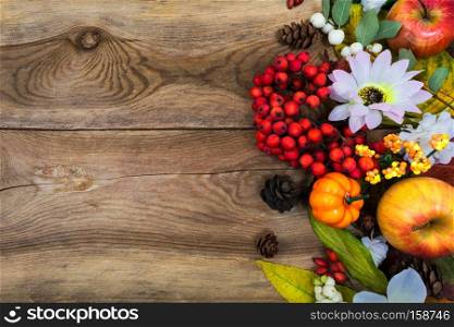 Thanksgiving or fall greeting background with small pumpkins, apples, rowan berries and white flowers on the old wooden table, copy space